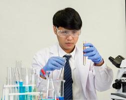 Aziatisch mannetje leerling wetenschapper in reagens menging laboratorium in een wetenschap Onderzoek laboratorium met test buizen van divers maten en microscopen. Aan de tafel in laboratorium chemie laboratorium wit achtergrond. foto