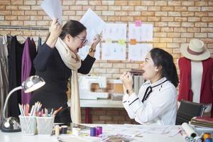 Aziatisch middelbare leeftijd vrouw mode ontwerper en jong tiener stagiair kleermaker vieren en vrolijk met jurk ontwerp werk succes, bevredigen samen in studio, gelukkig kostuum winkel klein bedrijf. foto