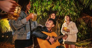 portret van gelukkig Aziatisch groep van vrienden hebben pret naar muziek- dining en drinken samen buitenshuis - gelukkig vrienden groep roosteren bieren - mensen, voedsel, drinken levensstijl, nieuw jaar viering concept. foto