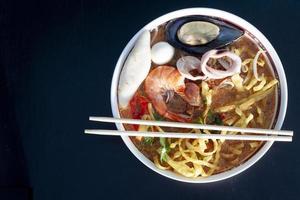 Thailand noodle Tom yam zee voedsel mee krob met pittig soep en vlees van garnalen, schaaldieren, inktvis en vlees bal Aan houten zwart kleur vloer. foto