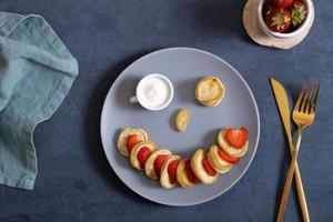 klein pannekoeken met aardbeien in de origineel portie in de het formulier van een smiley gezicht. top visie. vlak leggen foto