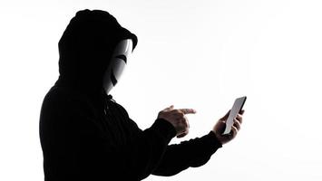 hacker anoniem en gezicht masker met smartphone in hand. Mens in zwart kap overhemd Holding en gebruik makend van mobiel telefoon Aan wit achtergrond. staan voor cyber misdrijf gegevens hacken of stelen persoonlijk gegevens concept foto