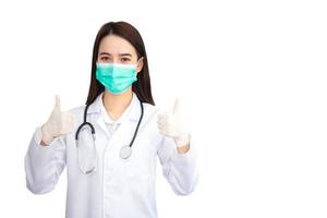 Aziatisch professioneel vrouw dokter wie draagt medisch jas en gezicht masker shows bonzen omhoog net zo mooi zo teken Aan een wit achtergrond in Gezondheid bescherming concept. foto