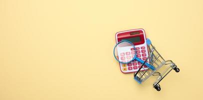 roze plastic rekenmachine in een miniatuur roze trolley Aan een geel achtergrond. begroting planning concept, spaargeld tellen foto