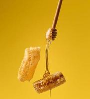 gieten transparant zoet honing van een houten stok Aan een was- honingraat. geel achtergrond. voedsel zweeft foto