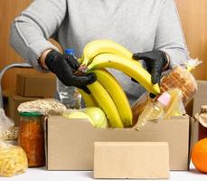 vrouw in een grijs trui is inpakken voedsel in een karton doos, de concept van bijstand en vrijwilligerswerk foto