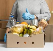 vrouw in handschoenen houdt verzamelen voedsel, fruit en dingen en een karton doos foto