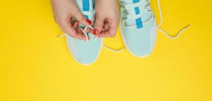 twee vrouw handen koppelverkoop veters Aan blauw textiel sportschoenen, top visie foto