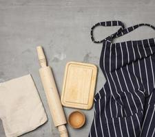 blauw gestreept chef schort, houten gereedschap Aan grijs achtergrond foto