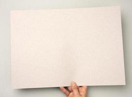 hand- houdt grijs blanco karton vel van papier, plaats voor opschrift foto
