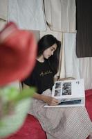 Aziatisch vrouw van Indonesië zit en leest een boek tegen een kleurrijk kleding achtergrond. foto