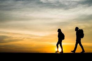 silhouetten van twee wandelaars met rugzakken die van de zonsondergang genieten foto