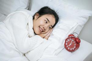 een vrouw die een wit overhemd draagt, liggend op haar bed met een wekker foto