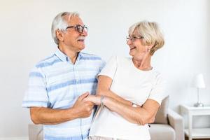 blij actief oud gepensioneerd romantisch paar dansen lachend in leven kamer, gelukkig midden- oud vrouw en ouderling man hebben pret Bij huis, glimlachen senior familie grootouders ontspannende bonding samen foto