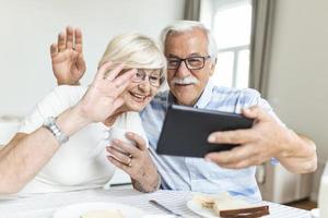 senior paar is pratend online via video verbinding Aan tablet. hebben mooi hoor tijd met vrienden en familie via video bellen.vasthouden hun handen samen foto