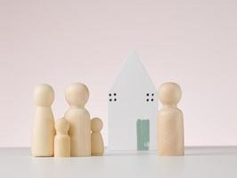 houten figuren van mannen en een miniatuur huis Aan een beige achtergrond. de concept van buying of verkoop echt landgoed, hypotheek en eigendom verzekering foto