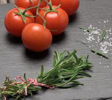 Fred tomaten en vers takje van rozemarijn met groen bladeren Aan een zwart achtergrond foto