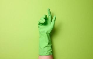 hand- in een rubber groen handschoen voor schoonmaak Aan een groen achtergrond, een deel van de lichaam is verheven omhoog foto