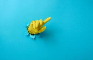hand- in een geel latex handschoen points een vinger Aan een blauw achtergrond. plaats voor opschrift van kortingen foto
