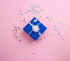 mooi blauw Gesloten doos met wit boog Aan een roze achtergrond met veelkleurig sparkles foto