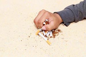 mannetje hand- verpletterd stapel sigaretten dichtbij omhoog Aan tafel terrazzo vloeren geel achtergrond. Gezondheid zorg concept hou op stoppen roken. foto