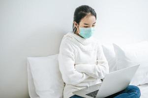 jonge vrouw draagt een masker zittend op haar bed foto