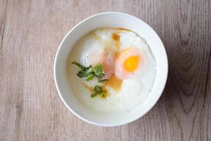 ei ontbijt , zacht gekookt eieren Aan wit kom met peper, koriander Aan houten tafel, onsen Tamago ei - ei magnetronoven foto