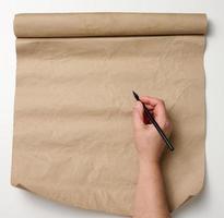 vrouw hand- houdt houten potlood over- bruin papier rollen Aan wit tafel. plaats naar schrijven tekst, lijst foto