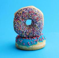 twee ronde gebakken donut met gekleurde suiker hagelslag en met blauw suiker suikerglazuur foto