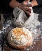 gebakken ronde brood Aan een bord, achter de koken in zwart kleren foto