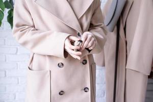 vrouw vervelend beige pastel jas, staand in de buurt kleren rek. garderobe verandering foto