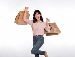 jong gelukkig Aziatisch vrouw met gewoontjes overhemd en denim jeans Holding boodschappen doen papier zak geïsoleerd Aan wit achtergrond foto