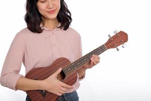 dichtbij omhoog van vrouw met gewoontjes kleding spelen ukulele geïsoleerd Aan wit achtergrond foto