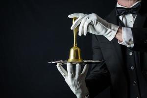 portret van butler in wit handschoenen en donker pak Holding goud klok Aan zilver dienblad. kopiëren ruimte voor onderhoud industrie en professioneel gastvrijheid. foto