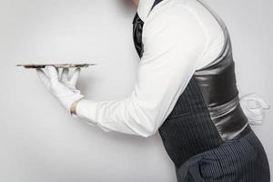 portret van butler of ober Holding zilver portie dienblad en buigen hoffelijk Aan wit achtergrond. professioneel gastvrijheid en wit handschoen onderhoud. foto