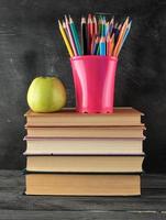 stack van boeken en een blauw schrijfbehoeften glas met veelkleurig houten potloden foto