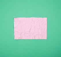 leeg verfrommeld roze rechthoekig vel van papier Aan een groen achtergrond foto
