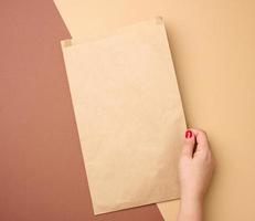 hand- Holding een leeg papier zak van bruin kraft papier Aan een bruin achtergrond, dichtbij omhoog foto