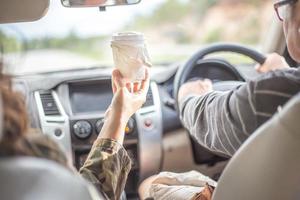 een vrouw die haar vriend in de auto een kop warme koffie serveert