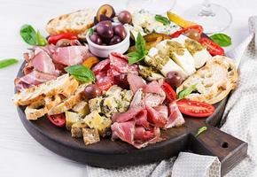 antipasto schotel met ham, prosciutto, salami, blauw kaas, Mozzarella met pesto en olijven Aan een houten achtergrond. foto