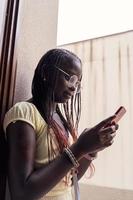 millennium Afrikaanse tiener is chatten met smartphone Aan de deur van de huis foto