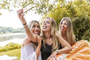 vrouw millennial vriendinnetjes nemen een selfie buitenshuis Aan de rivier- foto