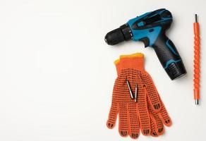 paar- van oranje textiel werk handschoenen en een portable boren Aan een accu liggen Aan een wit tafel foto
