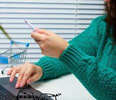 vrouw in een groen trui maakt aankopen online met een laptop, een credit kaart in hand. vrouw zittend Bij een wit tafel foto
