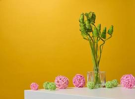 glas transparant vaas met groen droog bloemen Aan een wit tafel, geel achtergrond foto