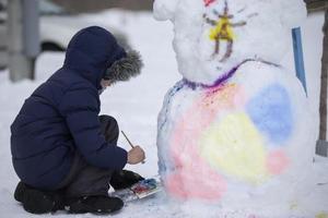 een jongen verven een sneeuwman Aan een winter dag. foto