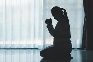 silhouet van vrouw geknield en bidden in modern kerk Bij zonsondergang tijd. vrouw Katholiek gebed aanbidden naar god wens een beter leven in huis Bij dageraad met van mening zijn vertrouwen. concept van aanbidders knielend. foto