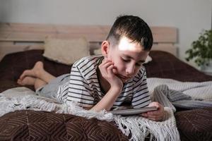 de jongen leugens Aan de bed en horloges een tekenfilms en video Aan een smartphone foto