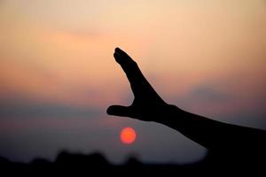 silhouet van menselijk hand- verheven naar maken een wens, zonsondergang achtergrond foto