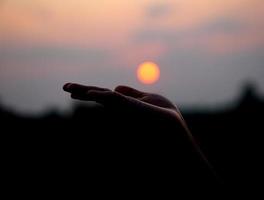 silhouet van menselijk hand- verheven naar maken een wens, zonsondergang achtergrond foto
